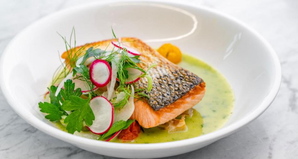 Pan-roasted salmon with pesto brodo garnished with parsley and radish