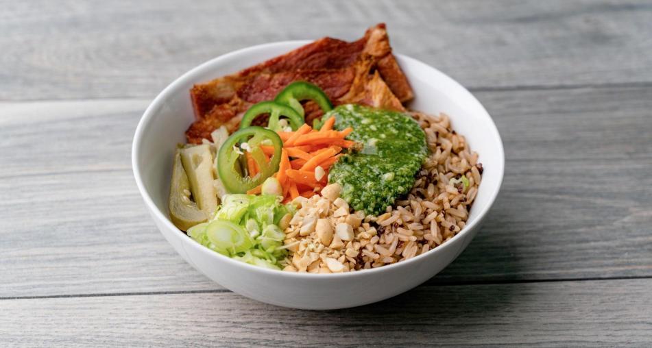 A bahn mi bowl containing jalapeños, carrots, rice, pork, and peanuts topped with Minor’s® Gluten Free GreenLeaf Basil Pesto