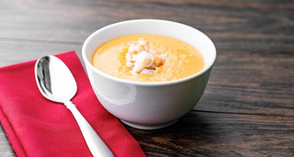 A bowl of shrimp and crab bisque next to a red cloth napkin and spoon