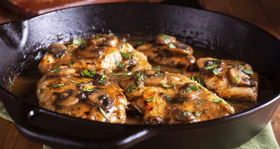 Chicken cooking in a pan with sauce, mushrooms, and chives
