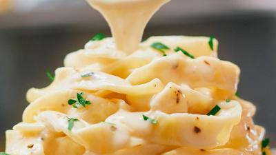 A spoon dripping vegan alfredo sauce onto a pasta dish