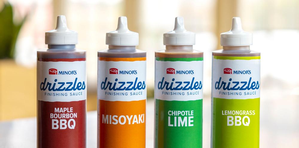 Four bottles of Minor's Drizzles Finishing sauces. Flavors shown: Maple Bourbon BBQ, Misoyaki, Chipotle Lim, and Lemongrass BBQ