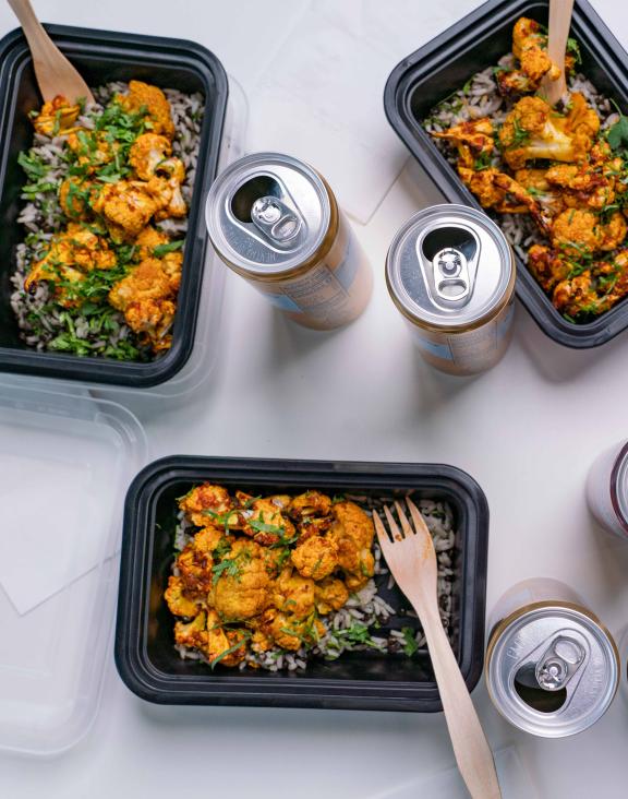 Overhead table shot of Masala Curry in takeout-style containers with cans of sparking water.
