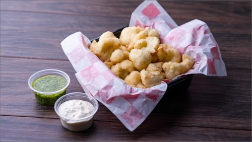 Country Fried Basil Pesto Cauliflower Bites in a takeout-style container with pesto and sour cream on the side