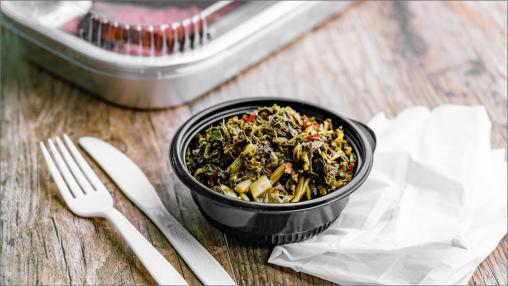 Southern Style Greens in a takeout-style container with plastic cutlery and napkin