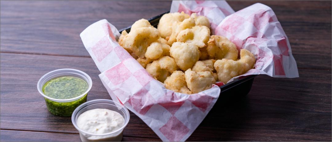 Country Fried Basil Pesto Cauliflower Bites in a takeout-style container with pesto and sour cream on the side