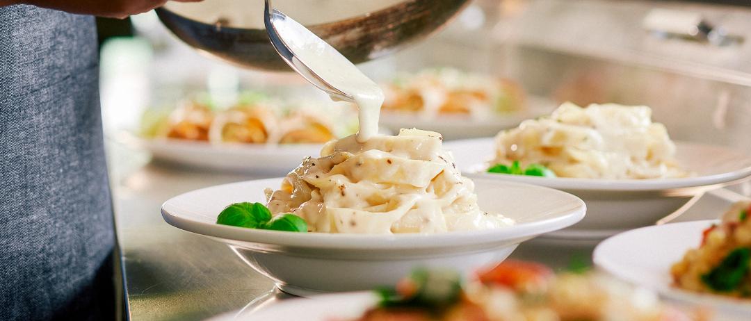 A person spooning vegan alfredo sauce from a pan onto a dish