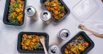 Overhead table shot of Masala Curry in takeout-style containers with cans of sparking water.
